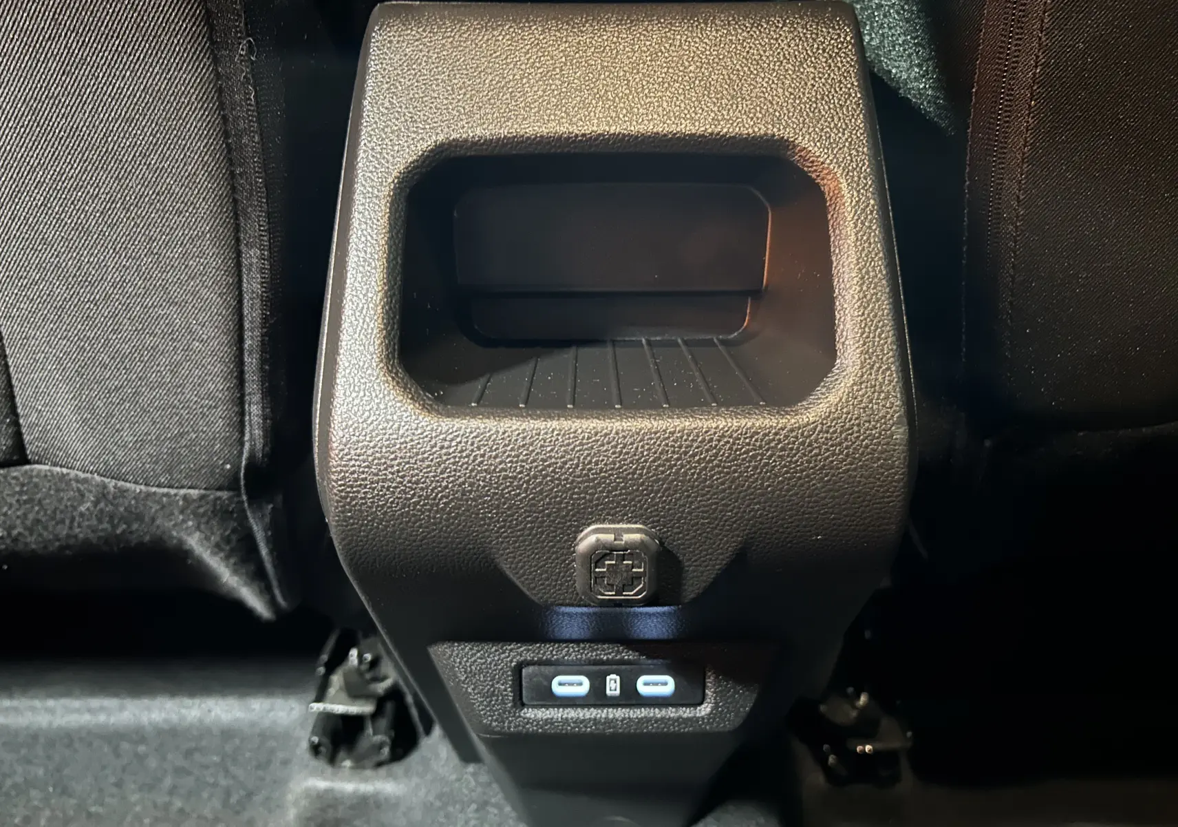 Gros plan sur la console arrière noire du Dacia Duster 2024 avec prises USB-C et rangement intégré.