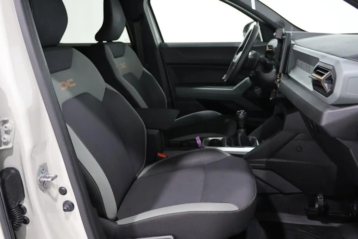 Vue intérieure côté conducteur du Dacia Duster 2024 avec sièges tissu bi-ton et tableau de bord moderne.