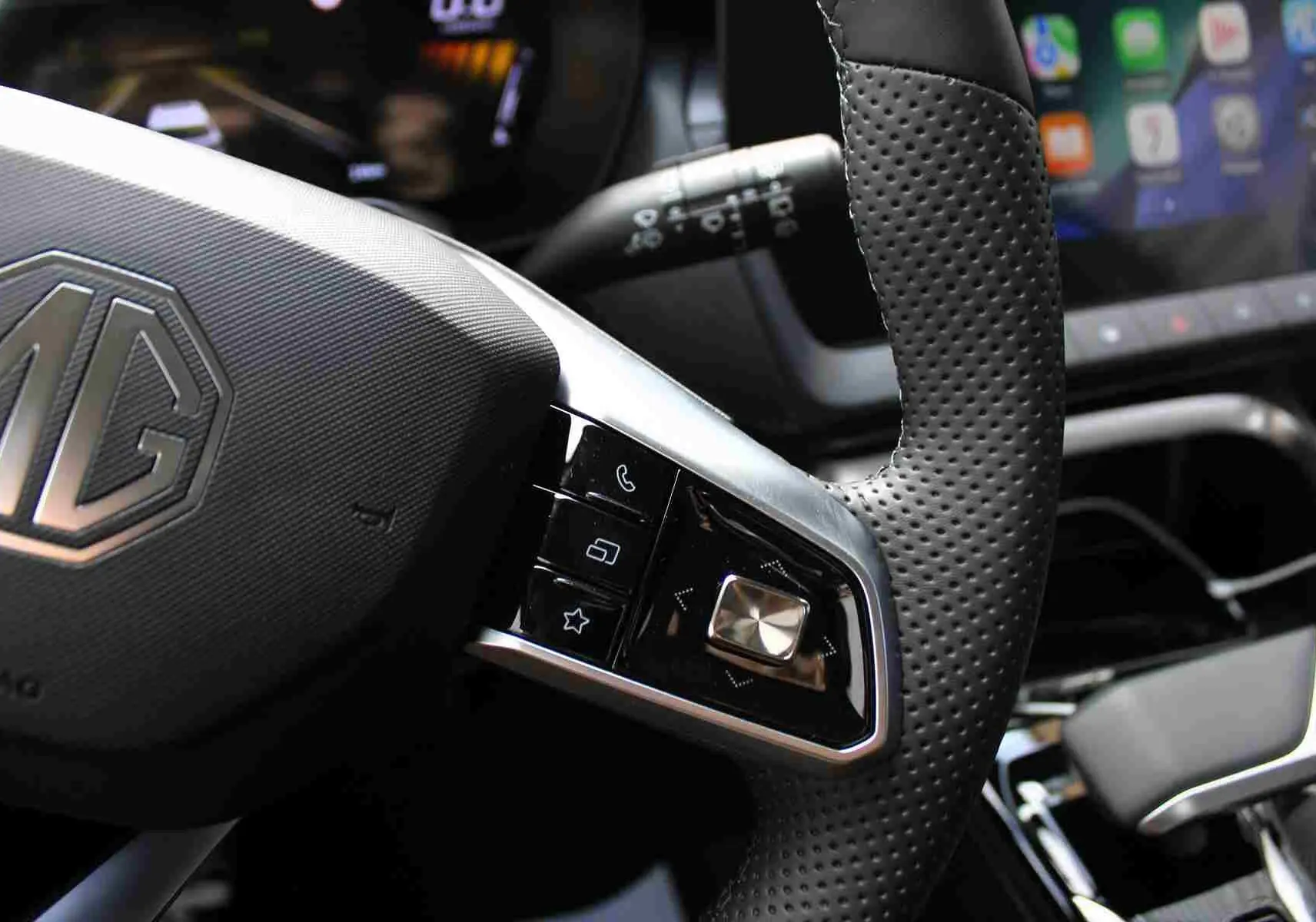 Gros plan sur le volant perforé et les commandes multifonctions du MG ZS hybride, intérieur gris et noir visible.