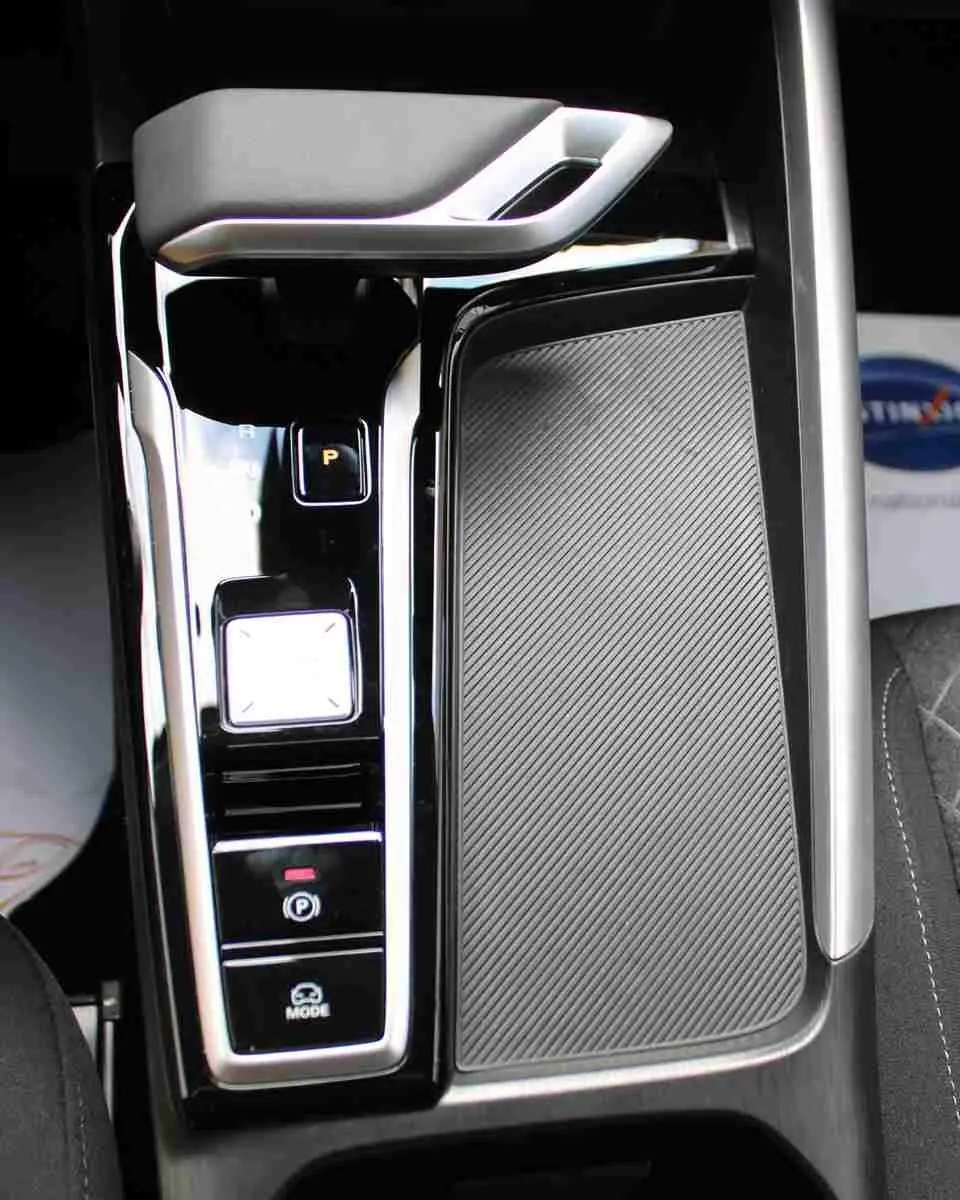 Vue en plongée sur la console centrale noire brillante du MG ZS 1.5L Hybrid+ avec levier de vitesses électronique et surface texturée.