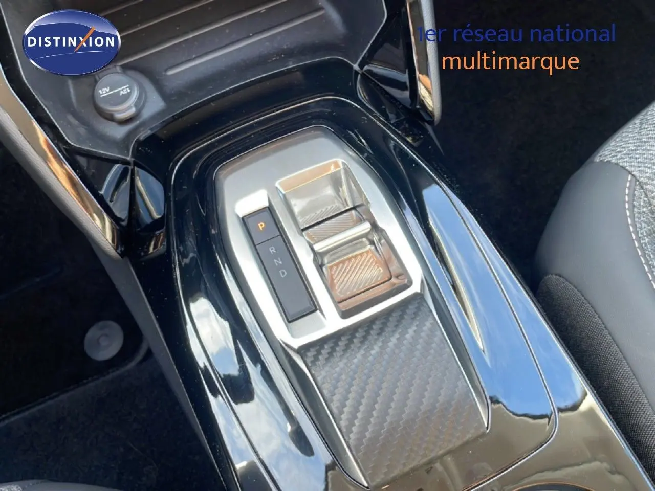 Gros plan sur la console centrale noire brillante de la Peugeot 208 Hybrid 110ch avec commande de boîte auto et insert effet carbone.