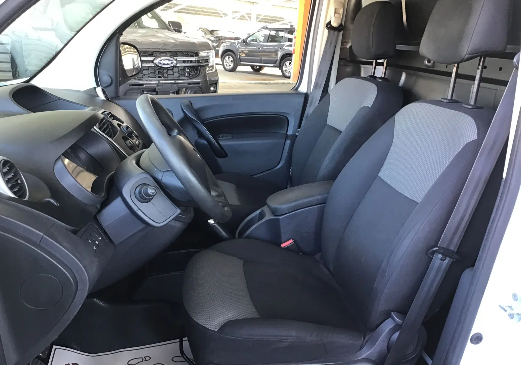 Vue intérieure côté conducteur du Renault Kangoo blanc 2021, montrant les sièges avant et le tableau de bord noir.