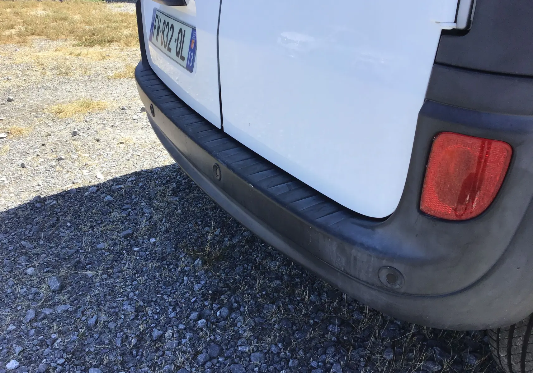 Gros plan sur le pare-chocs arrière noir et la porte blanche du Renault Kangoo 1.5 Blue dCi, avec feu arrière droit visible.