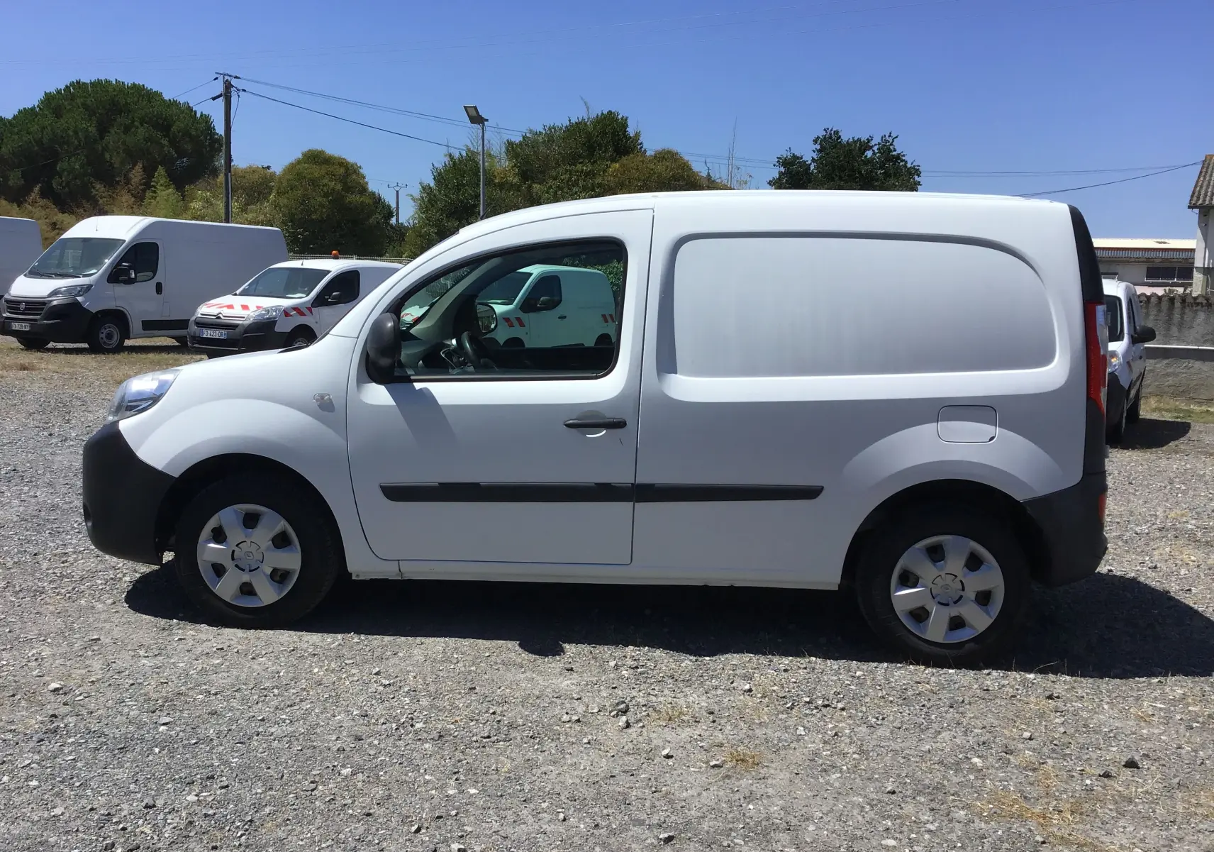 Vue de profil côté gauche d’un utilitaire Renault Kangoo blanc, avec porte latérale pleine et jantes acier.