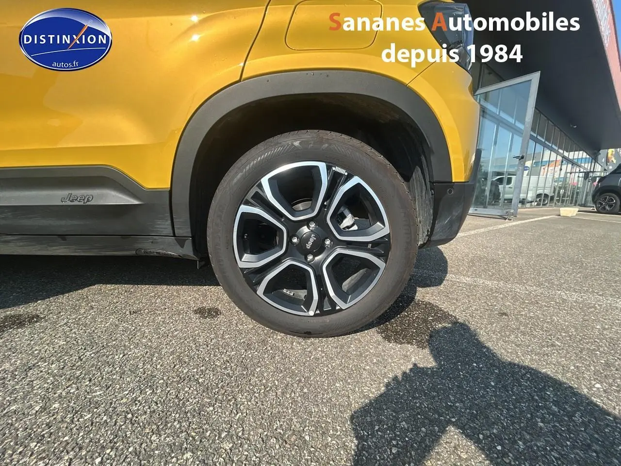 Gros plan sur la roue avant droite d’un Jeep Avenger jaune foncé avec logo Jeep sur le bas de caisse.