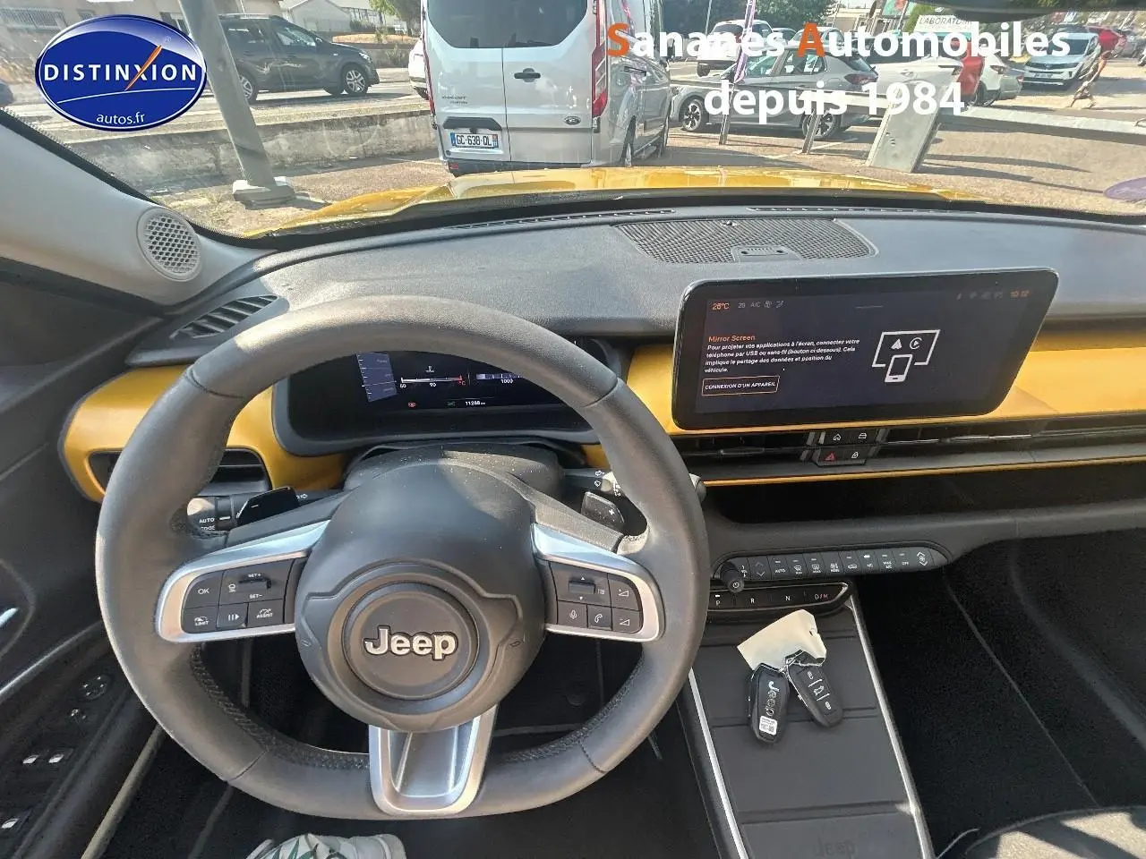 Vue intérieure du tableau de bord et volant Jeep Avenger jaune foncé, avec écran tactile et clés sur la console centrale.