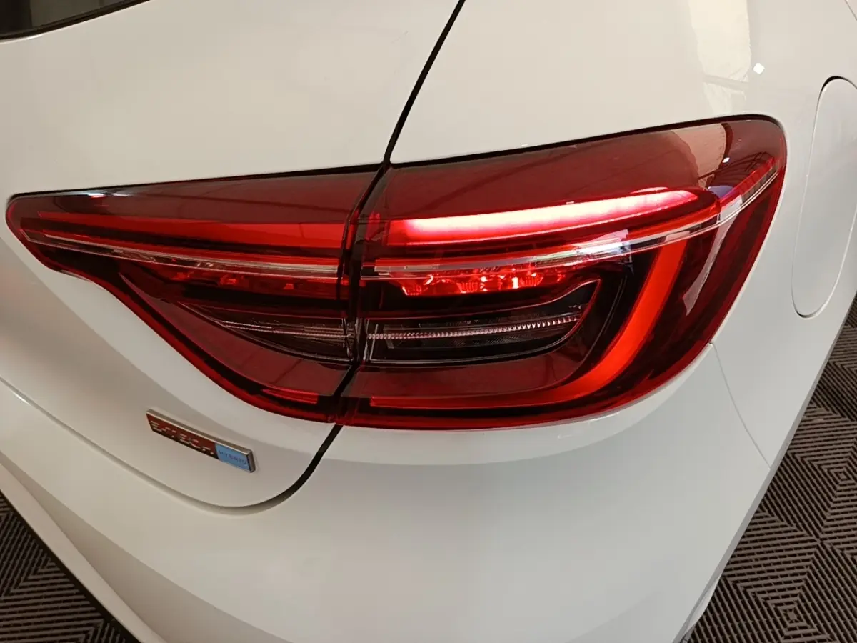 Gros plan sur le feu arrière droit rouge d’une Renault Clio Business E-TECH blanche, avec badge hybride visible.