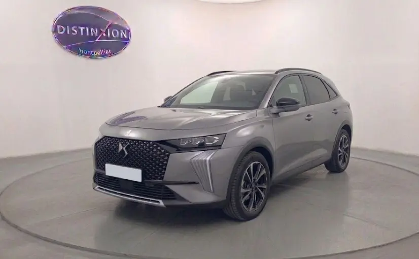Vue 3/4 avant d'un DS7 2025 gris métallisé avec calandre distinctive et jantes noires dans un studio.