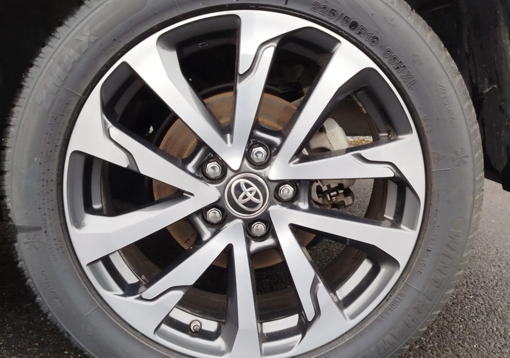 Gros plan sur la jante alliage bi-ton argent et noir avec logo Toyota, montée sur un pneu 225/50 R18 du Corolla Cross noir.