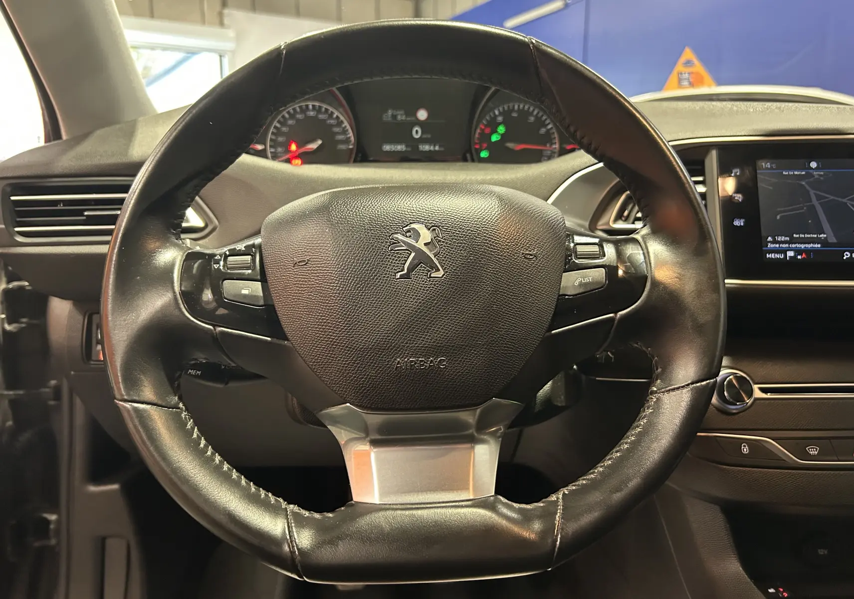 Gros plan sur le volant en cuir noir de la Peugeot 308 Active Pack 2021, avec tableau de bord et écran tactile visibles.