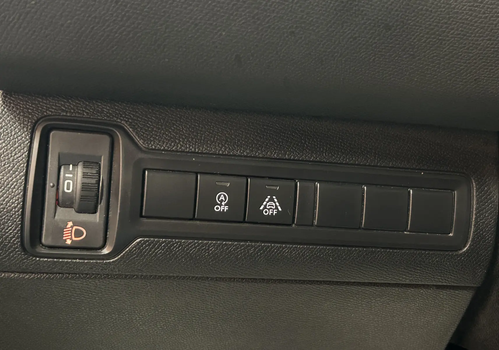 Gros plan sur les commandes noires du tableau de bord de la Peugeot 308 Active Pack gris, avec réglage phares et boutons d'assistance éteints.