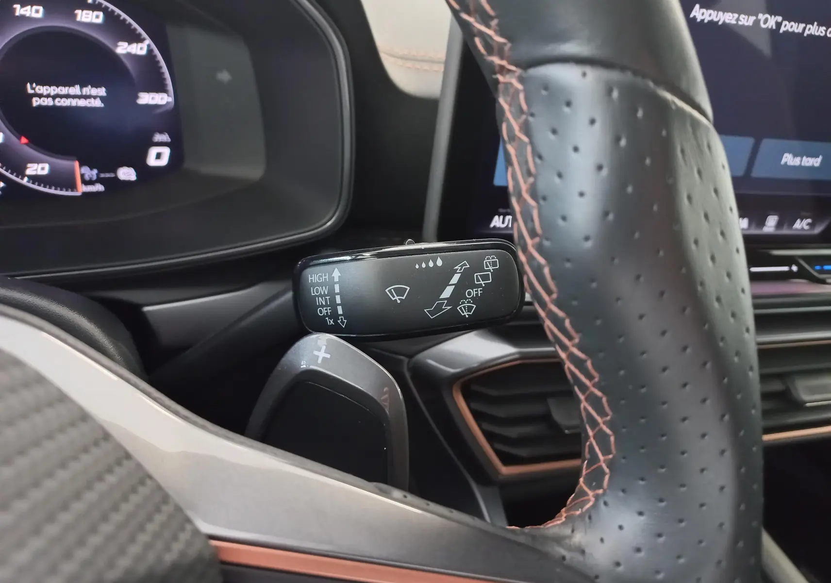 Gros plan sur le commodo d’essuie-glace et le volant perforé avec surpiqûres orange d’une CUPRA Leon blanc Nevada, intérieur moderne.