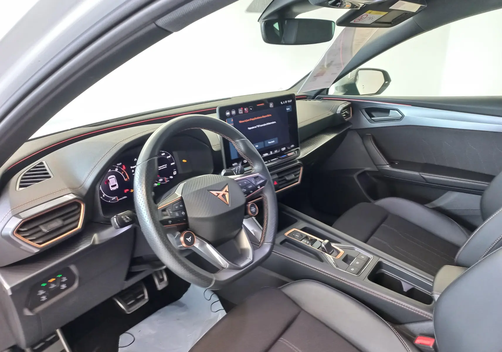 Vue intérieure côté conducteur de la CUPRA Leon 2025 avec volant multifonction, écran tactile et finitions noires avec surpiqûres cuivrées.