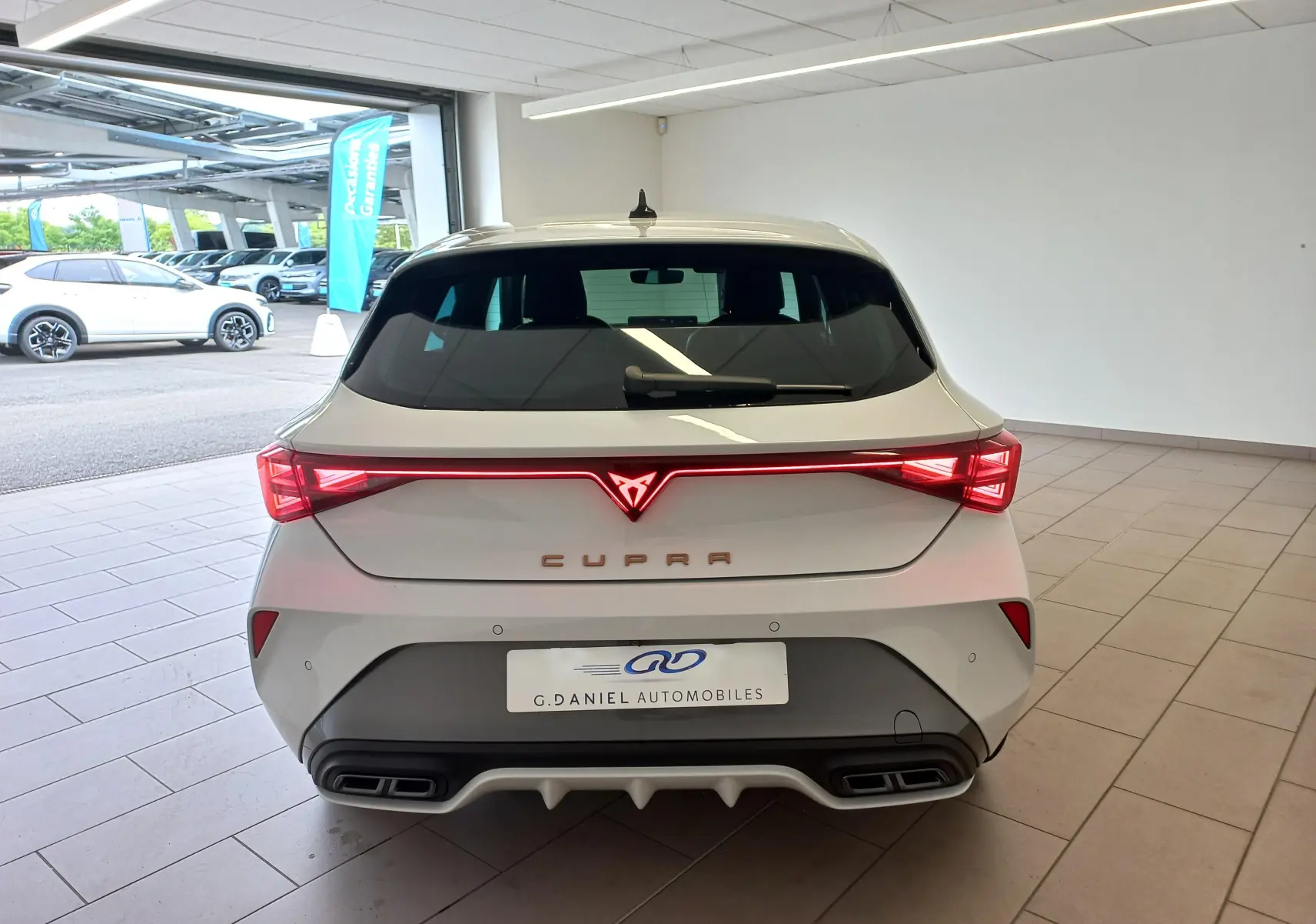 Vue arrière d'une CUPRA Leon blanche Nevada 2025 avec feux LED reliés et double sortie d'échappement intégrée.