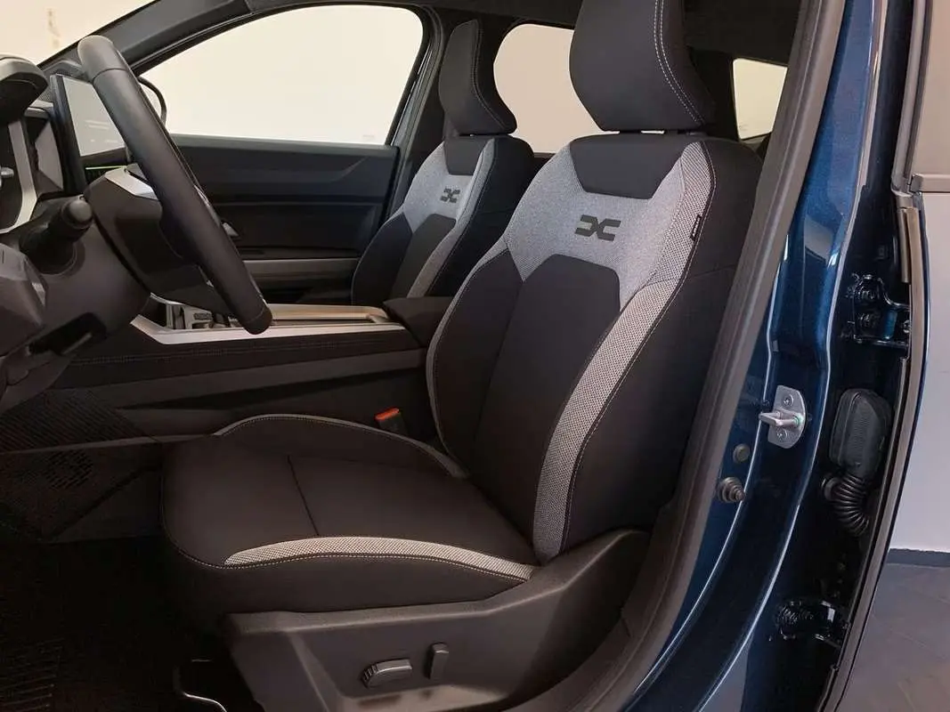 Vue intérieure côté conducteur du Dacia Bigster Hybrid 155 Journey Plus bleu indigo, sièges tissu noir et gris avec logo brodé.