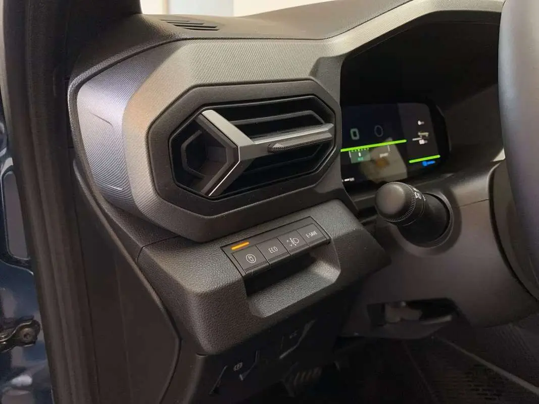 Gros plan sur la console gauche du tableau de bord du Dacia Bigster bleu indigo, avec commandes et aérateur hexagonal.