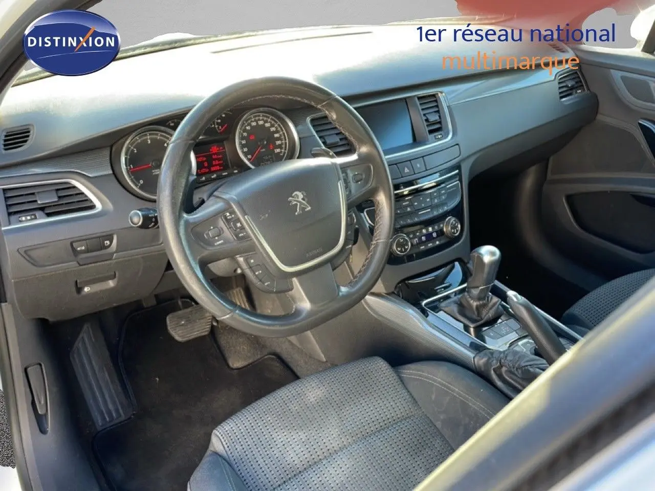 Vue intérieure côté conducteur du tableau de bord et volant noir d'une Peugeot 508 blanche de 2012 avec boîte automatique.