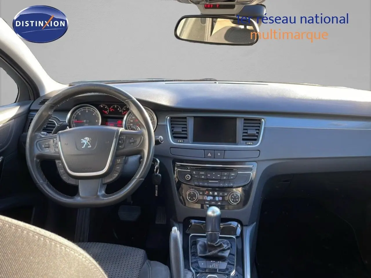 Vue intérieure avant du tableau de bord et du volant noir de la Peugeot 508 blanche, avec console centrale et écran tactile éteint.
