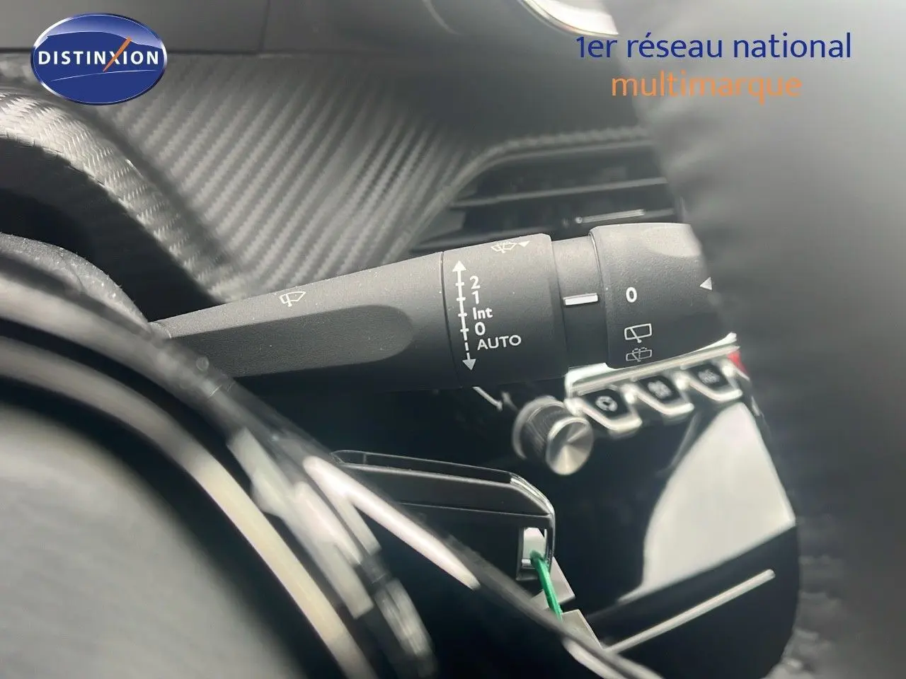 Gros plan sur la commande d'essuie-glace à gauche du volant dans l'habitacle d'un Peugeot 2008 blanc Okenite Metal.
