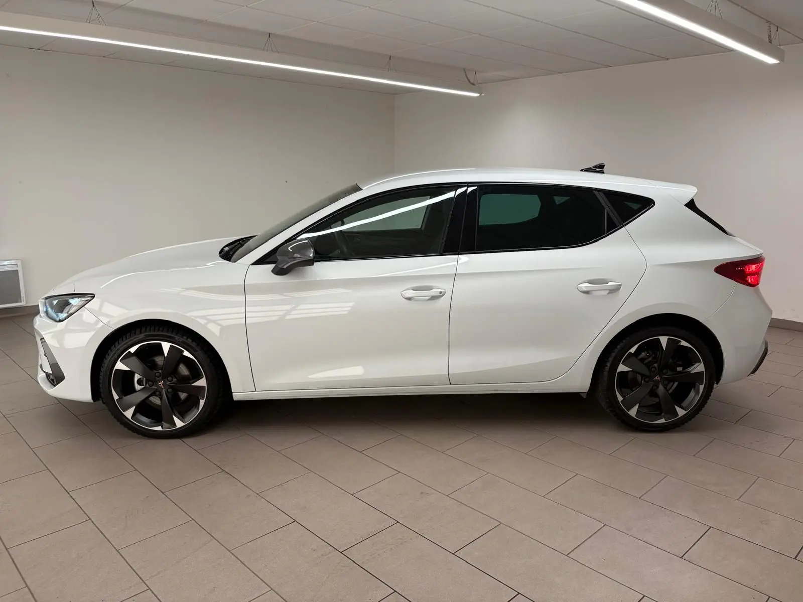 Vue de profil côté gauche d'une CUPRA Leon blanche Nevada 2025 avec jantes noires et vitres teintées.