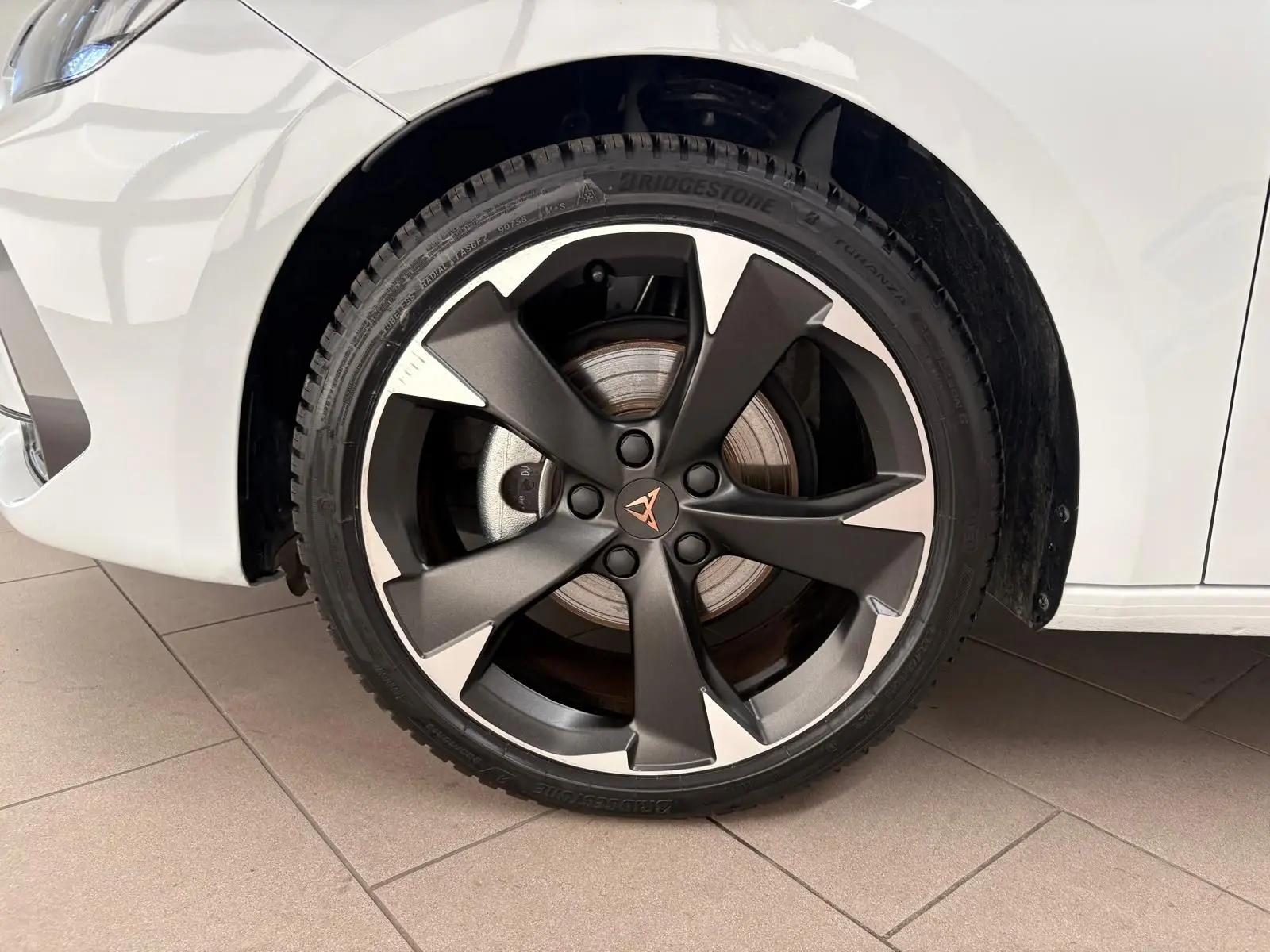 Gros plan sur la roue avant droite d'une CUPRA Leon blanc Nevada avec jante alliage sombre à cinq branches.