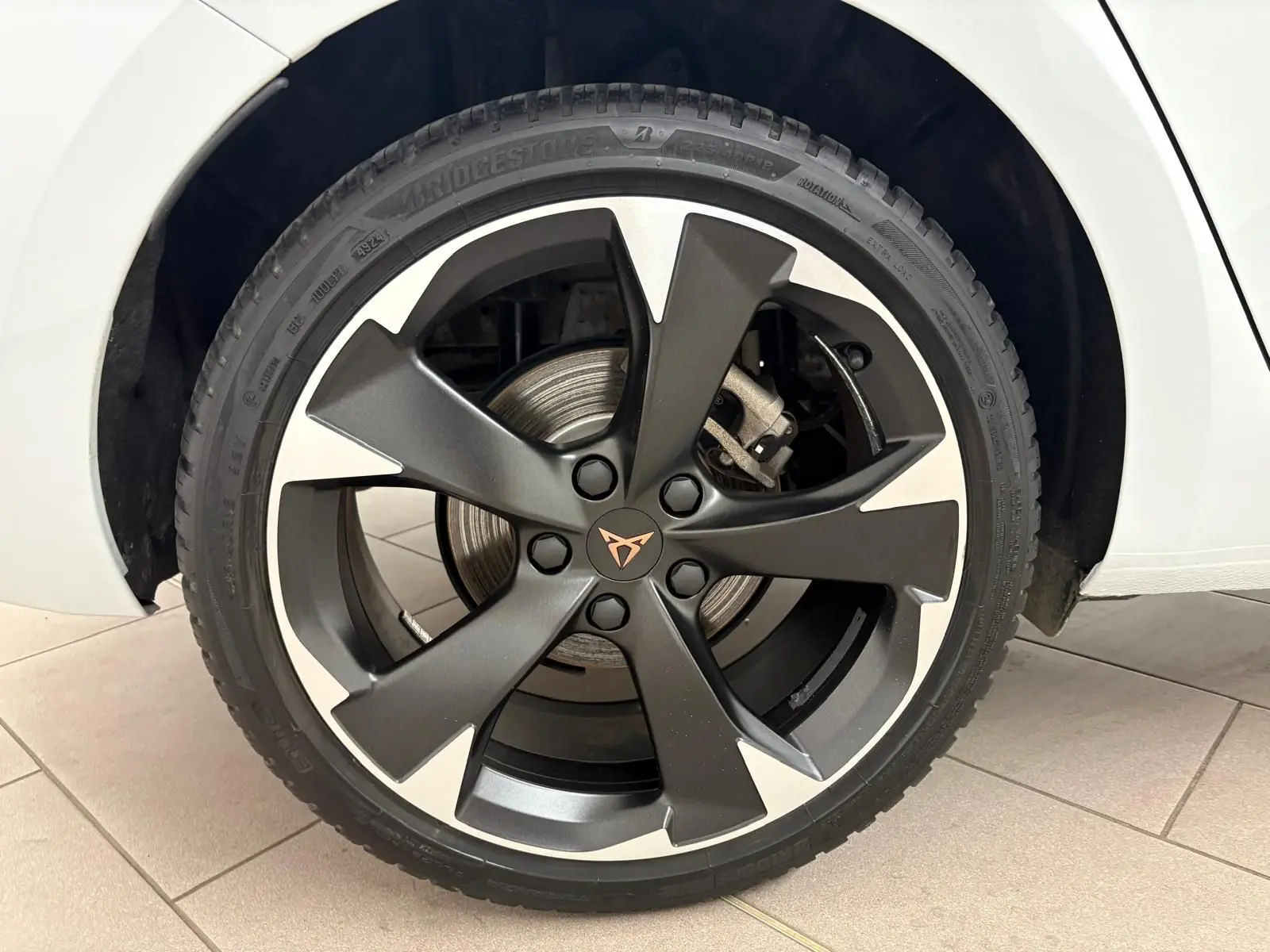 Gros plan sur la roue avant droite d'une CUPRA Leon blanc Nevada avec jante alliage noire et argentée au design distinctif.