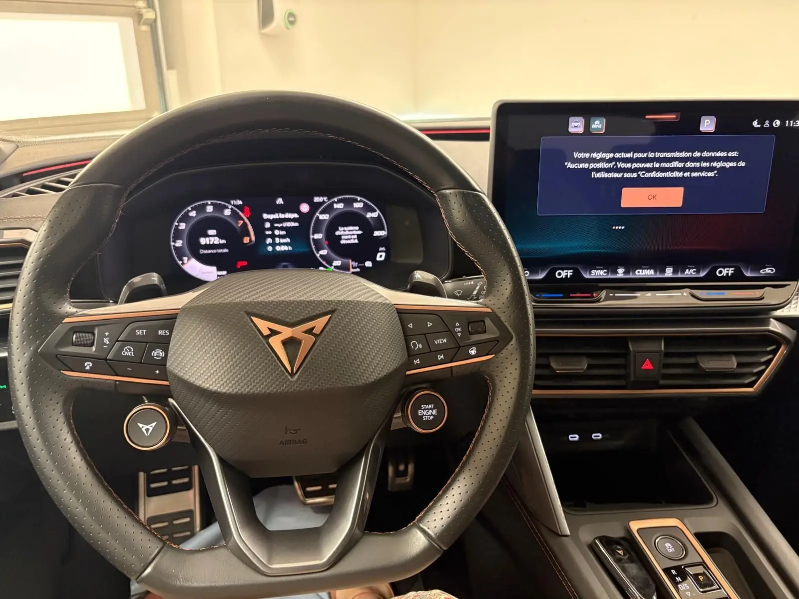 Vue intérieure centrée sur le volant CUPRA noir avec logo cuivré et tableau de bord numérique lumineux.