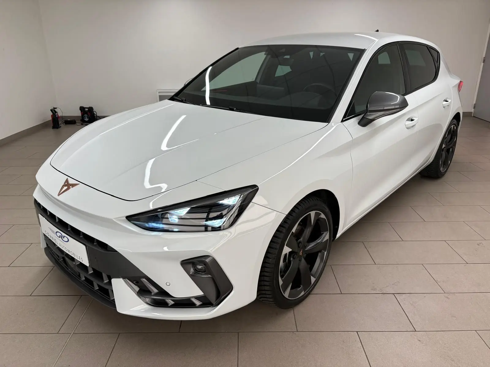 Vue 3/4 avant droit d'une CUPRA Leon Phase 2 blanche Nevada avec jantes noires et feux LED allumés.