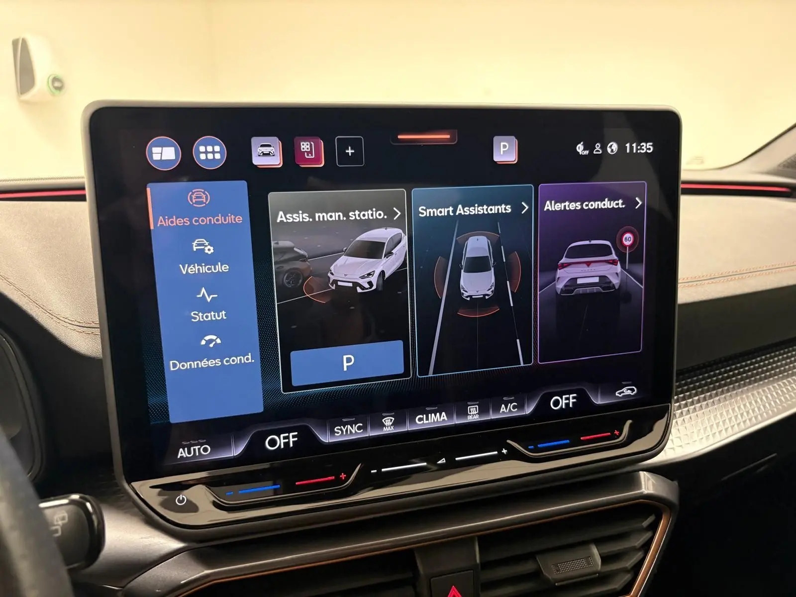 Écran tactile central du tableau de bord de la CUPRA Leon blanc Nevada, affichant les aides à la conduite et assistants intelligents.