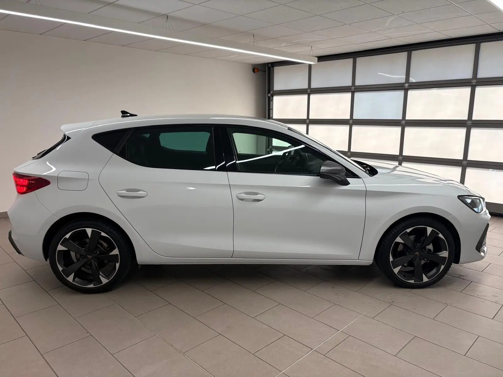 Vue de profil côté gauche d'une CUPRA Leon blanche Nevada 2025 avec jantes noires et vitres teintées.