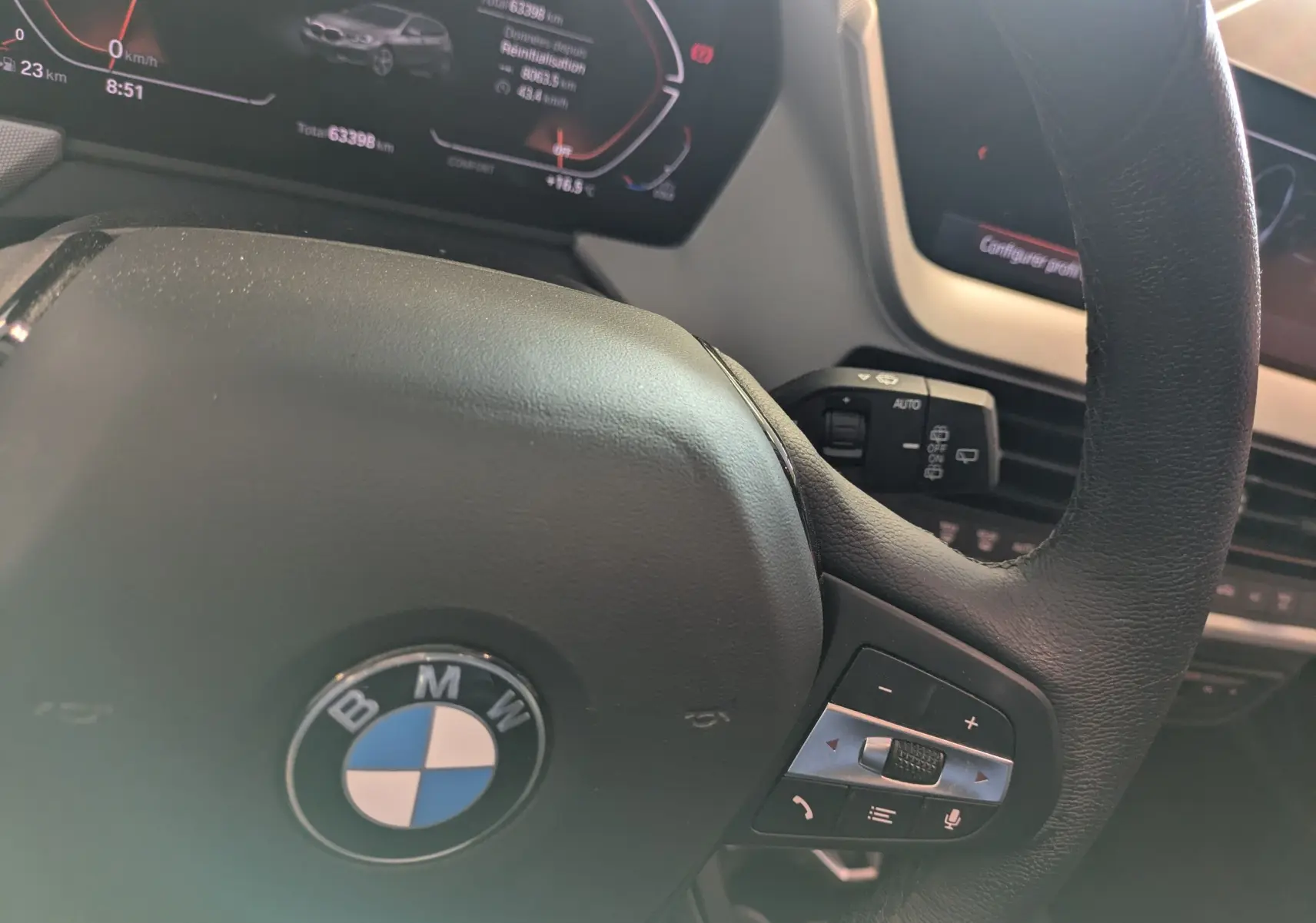 Vue rapprochée du volant cuir noir BMW Série 1 116d 2022 avec commandes intégrées et tableau de bord numérique.