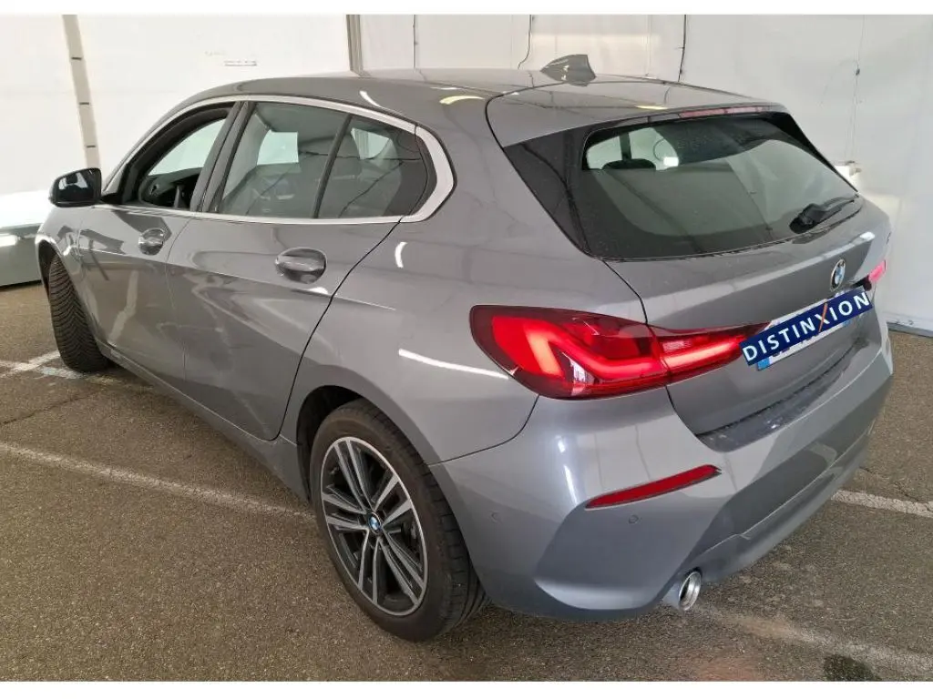 BMW Série 1 gris vue de profil côté gauche, avec jantes alliage et intérieur visible en showroom.