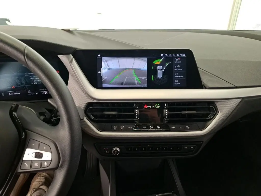 Coffre ouvert d’une BMW Série 1 gris montrant la roue de secours et les outils de bord rangés sous le plancher.