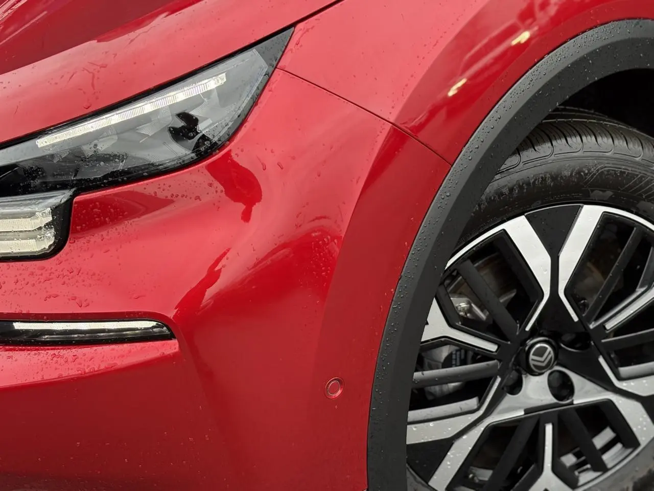 Gros plan sur l'avant droit rouge Elixir de la Citroën C4 Hybrid 2025 avec phares LED et jante alliage 18 pouces.