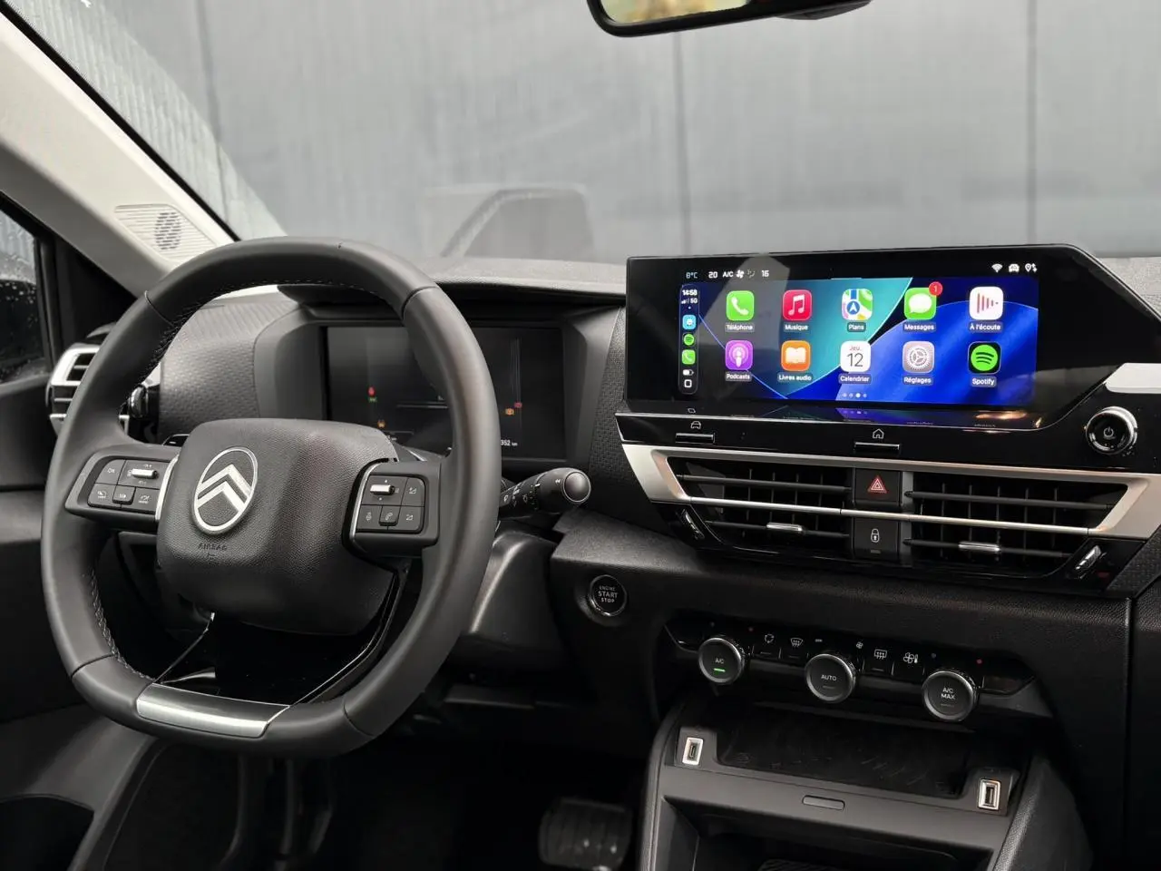 Vue intérieure du poste de conduite Citroën C4 Hybrid 2025, volant multifonction et écran tactile central lumineux.