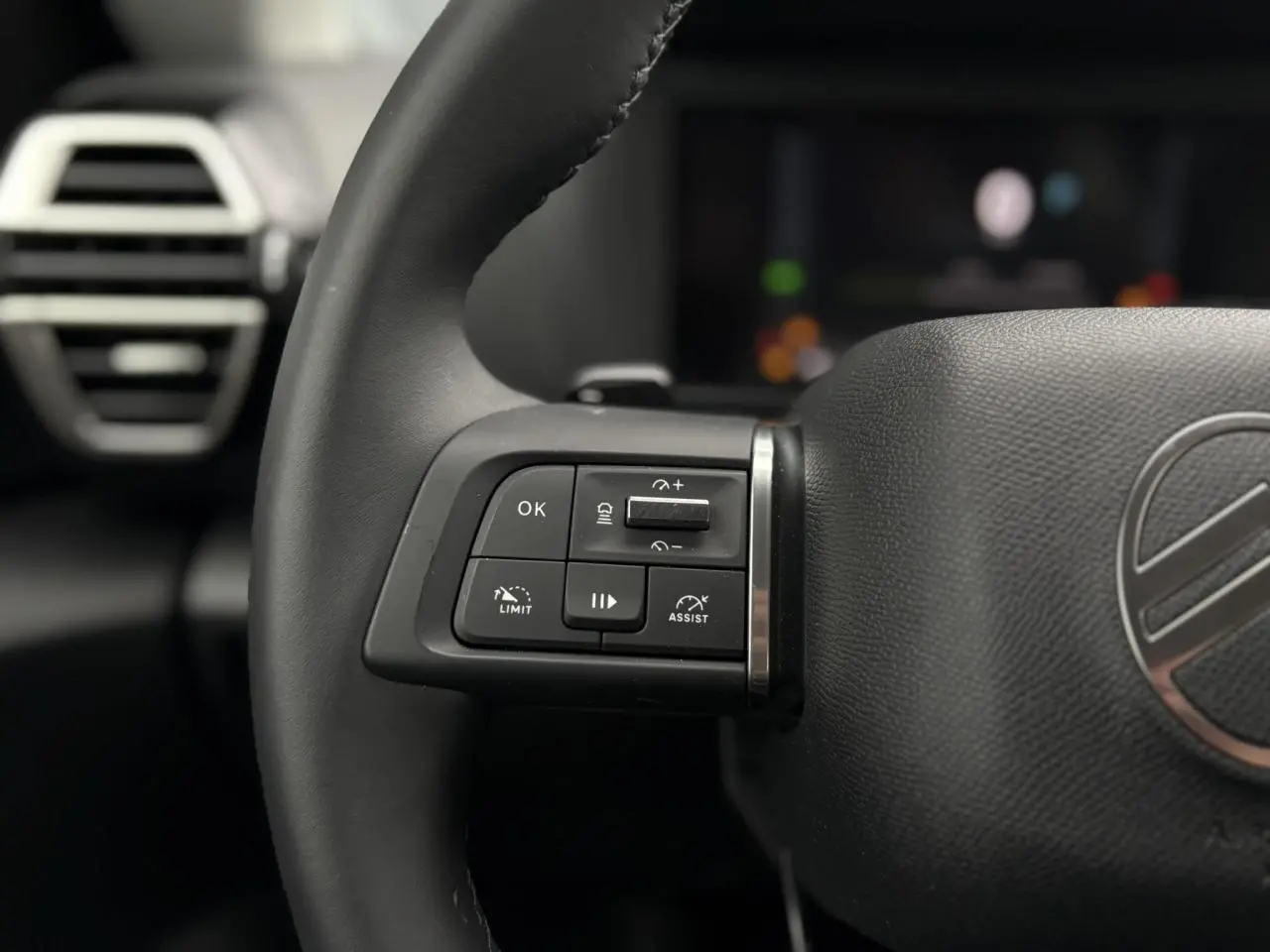 Gros plan sur les commandes au volant à gauche du Citroën C4 Hybrid 2025, cuir noir et logo Citroën visible.