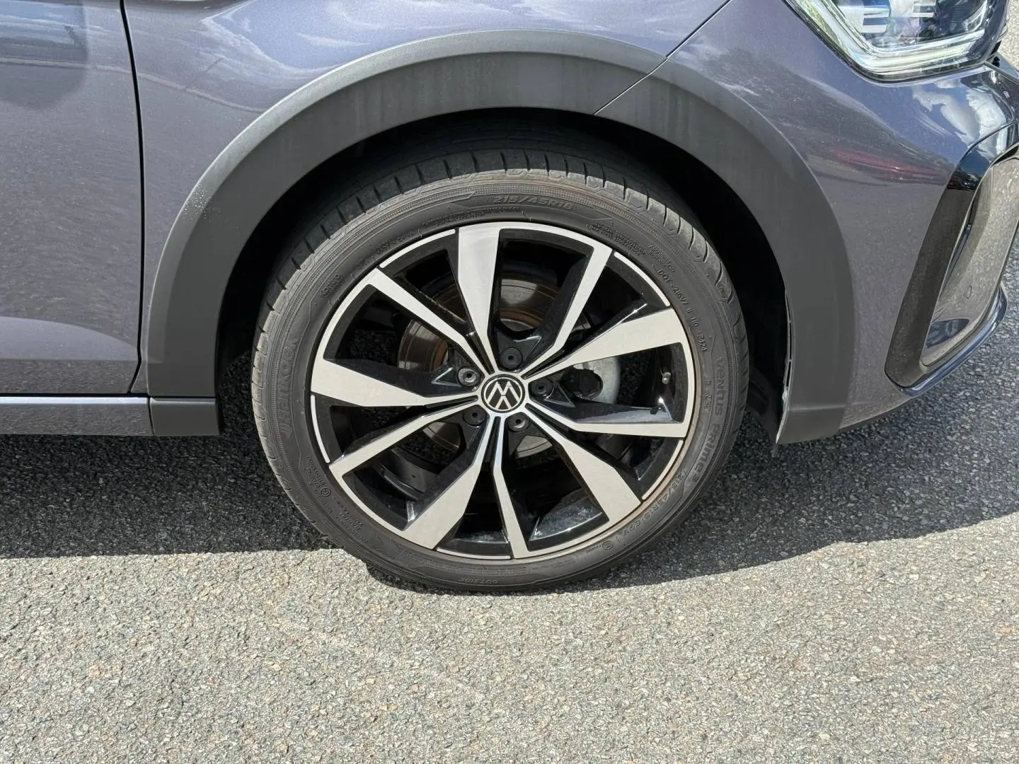 Gros plan sur la roue avant gauche du Volkswagen Taigo gris avec jante alliage noir et argentée en étoile.