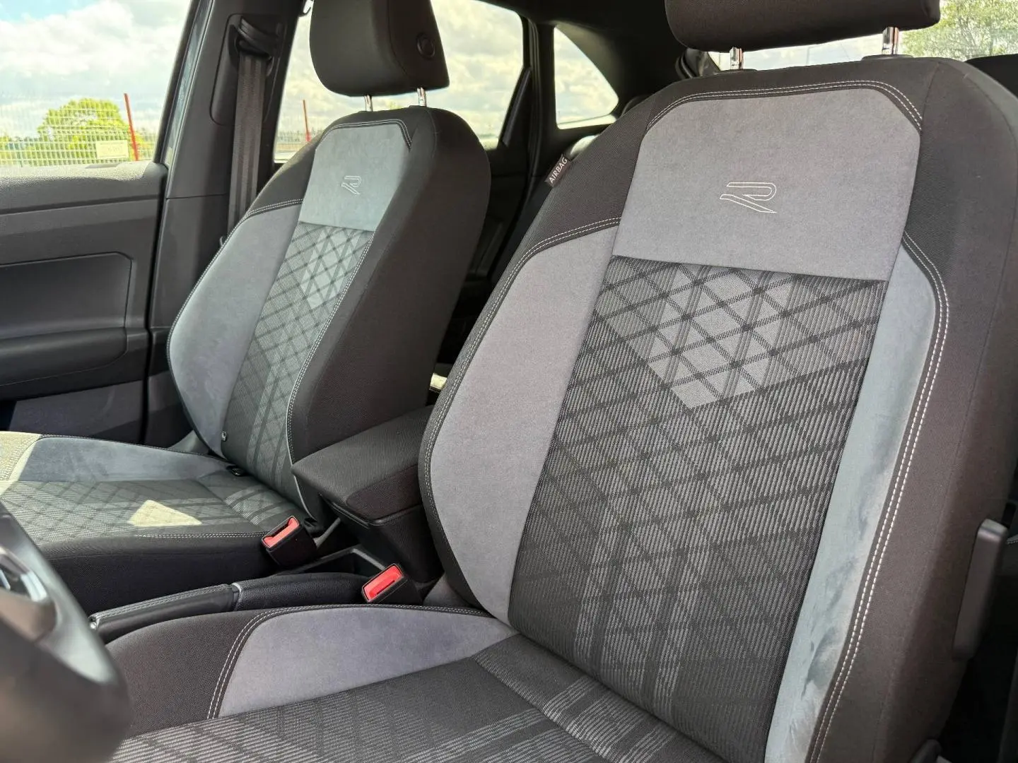 Vue intérieure rapprochée des sièges avant gris et noirs en tissu R-Line avec logo brodé sur Volkswagen Taigo 2025.