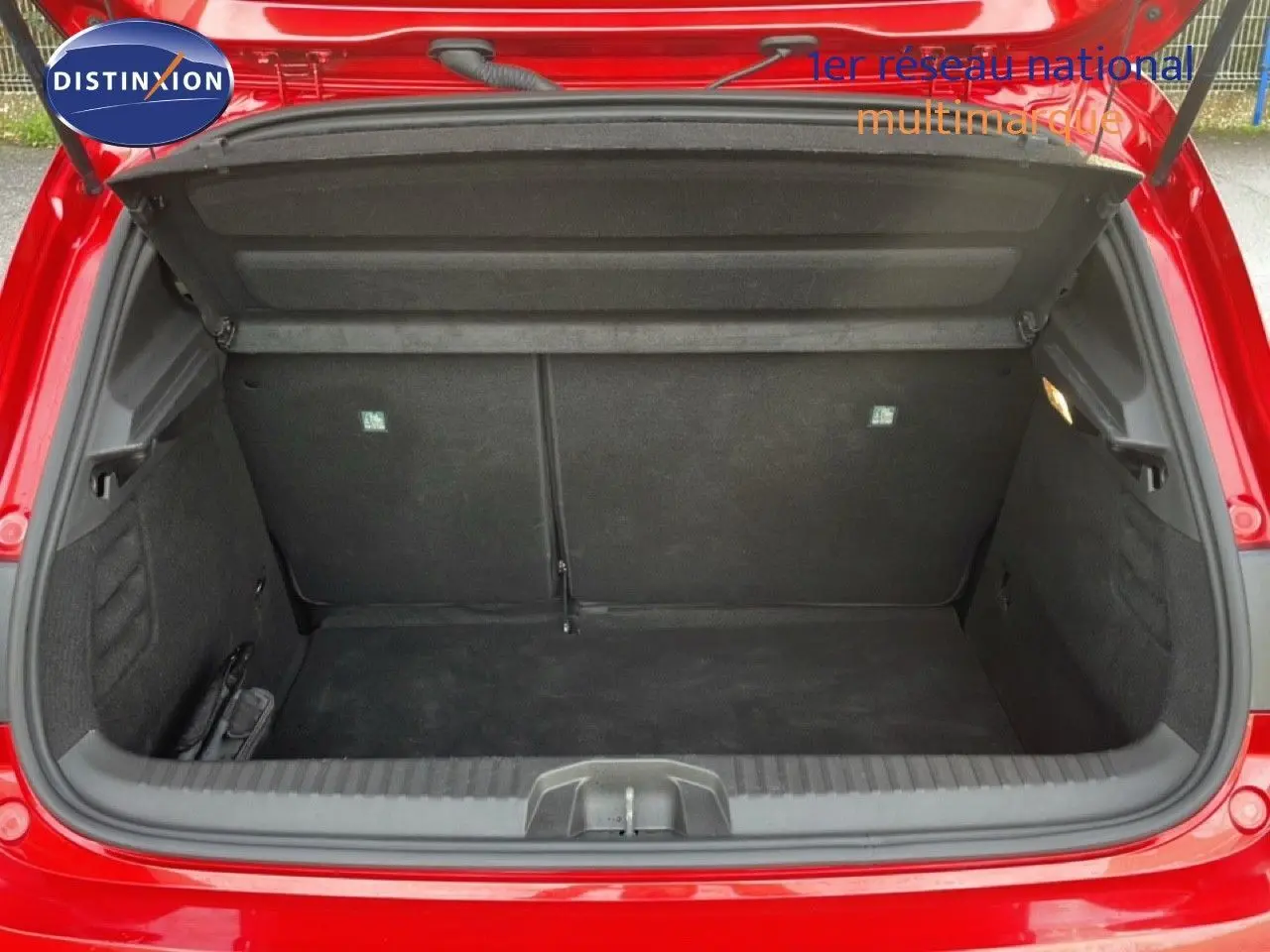 Coffre ouvert vu de l'arrière d'une Renault Clio rouge Désir métal, montrant l'espace de chargement vide.