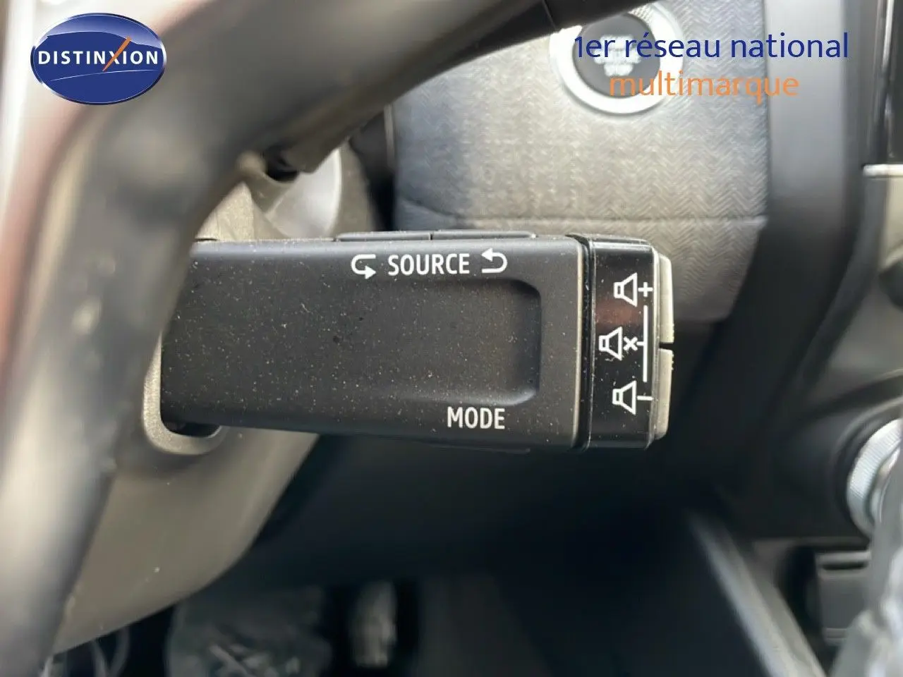 Gros plan sur la commande au volant de la Renault Clio 2025, boutons source et mode visibles, intérieur noir.