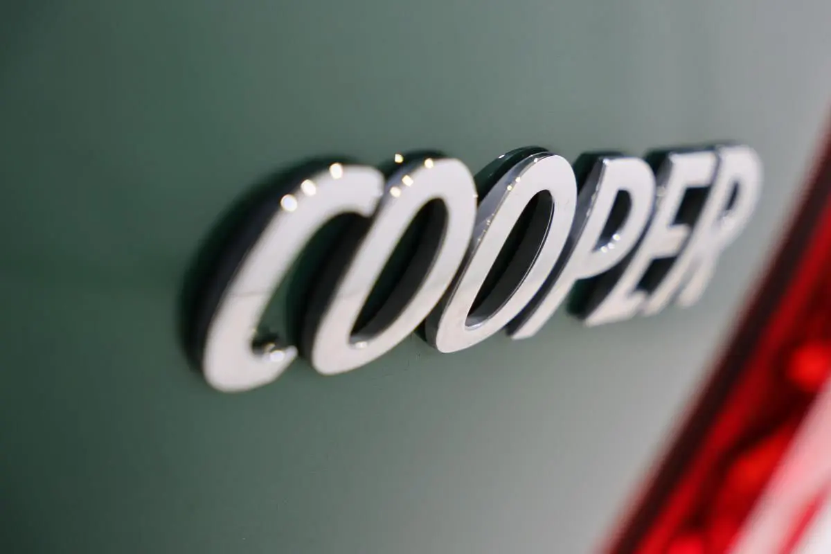 Gros plan sur l’inscription chromée Cooper sur la carrosserie vert métallisé d’un MINI Countryman, près du feu arrière rouge.