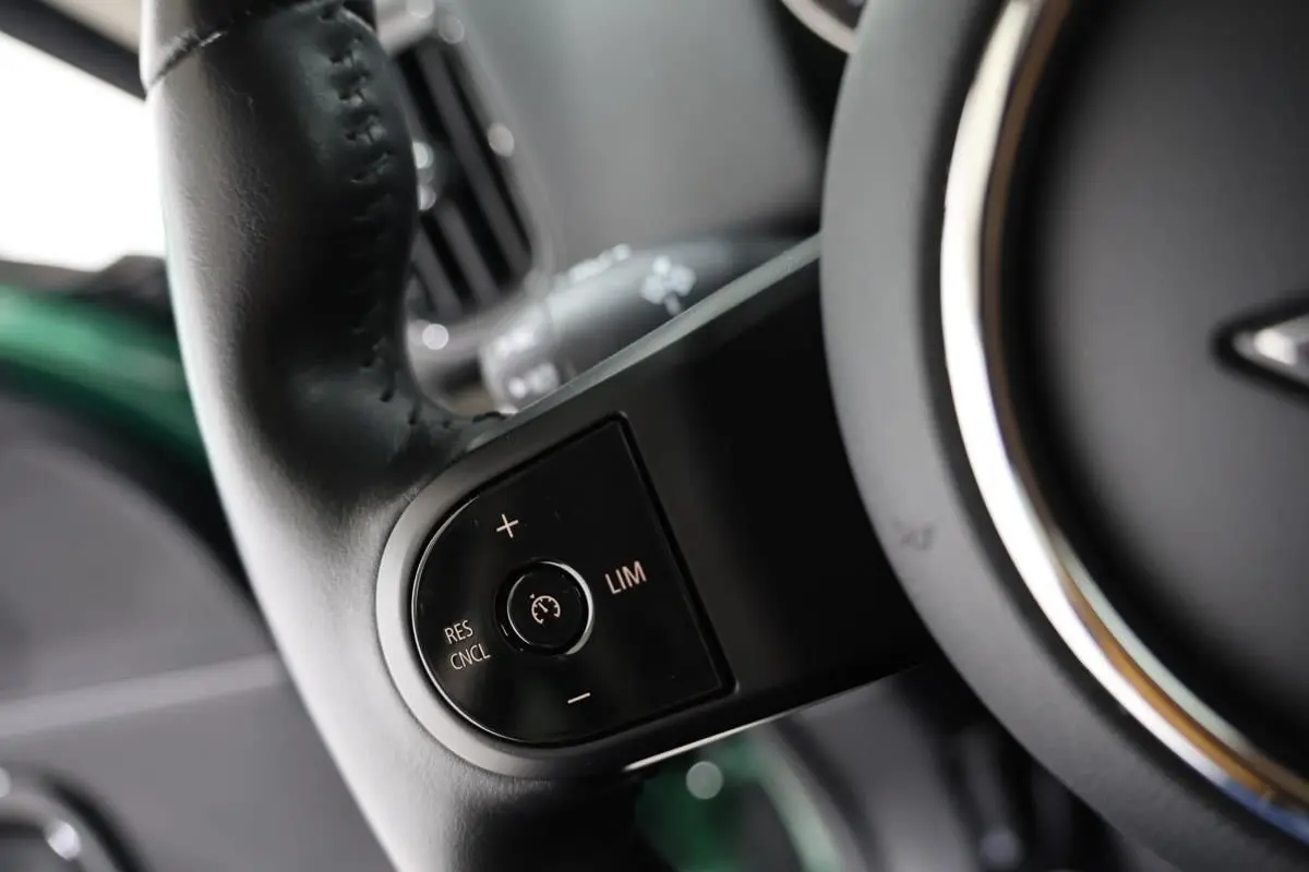 Gros plan sur les commandes de régulateur de vitesse au volant noir d’un MINI Countryman vert métallisé.