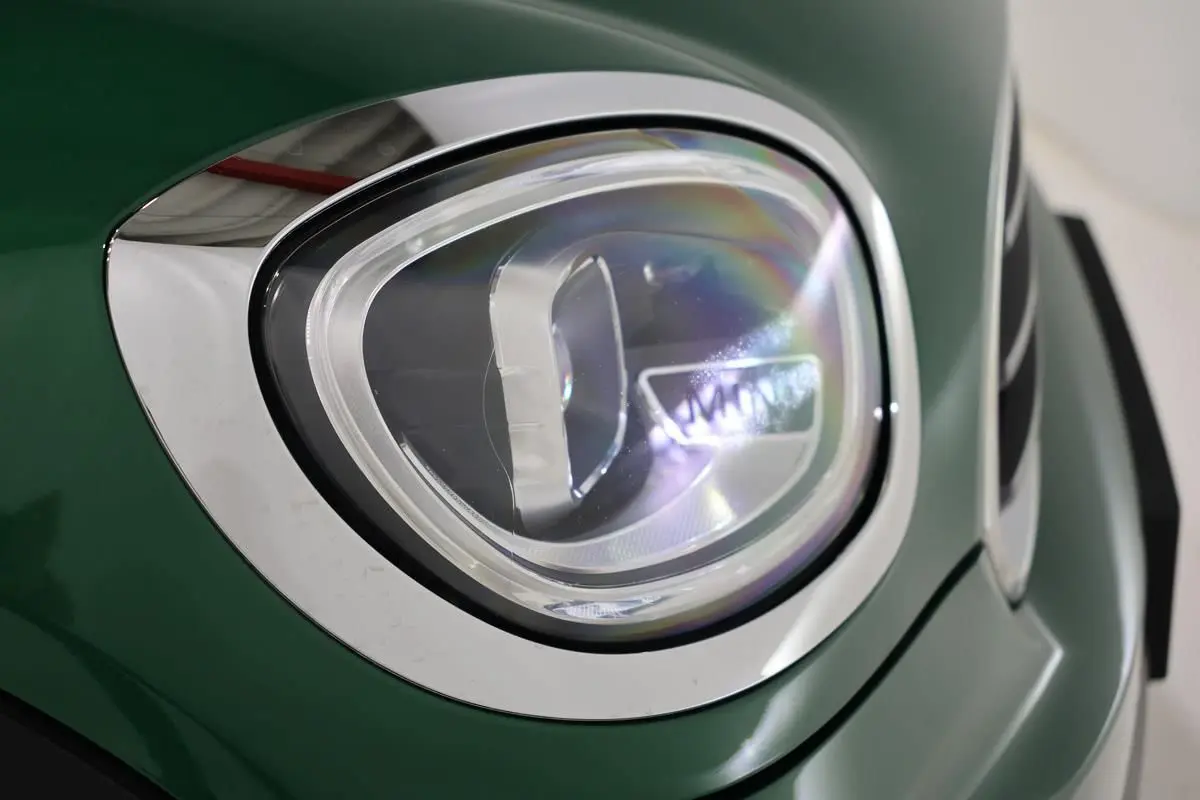 Gros plan sur le phare avant gauche d'une MINI Countryman vert métallisé avec contour chromé.