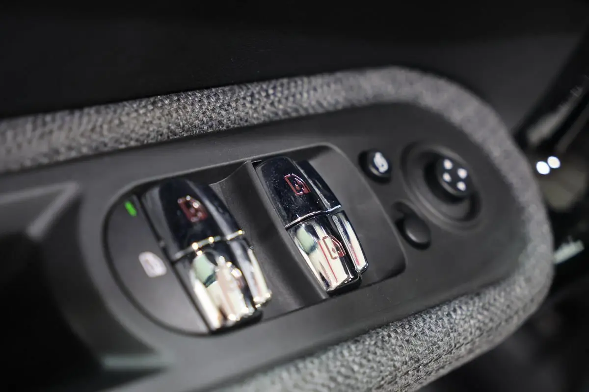 Gros plan sur les commandes chromées des vitres électriques et rétroviseurs, entourées de tissu gris dans une MINI Countryman.