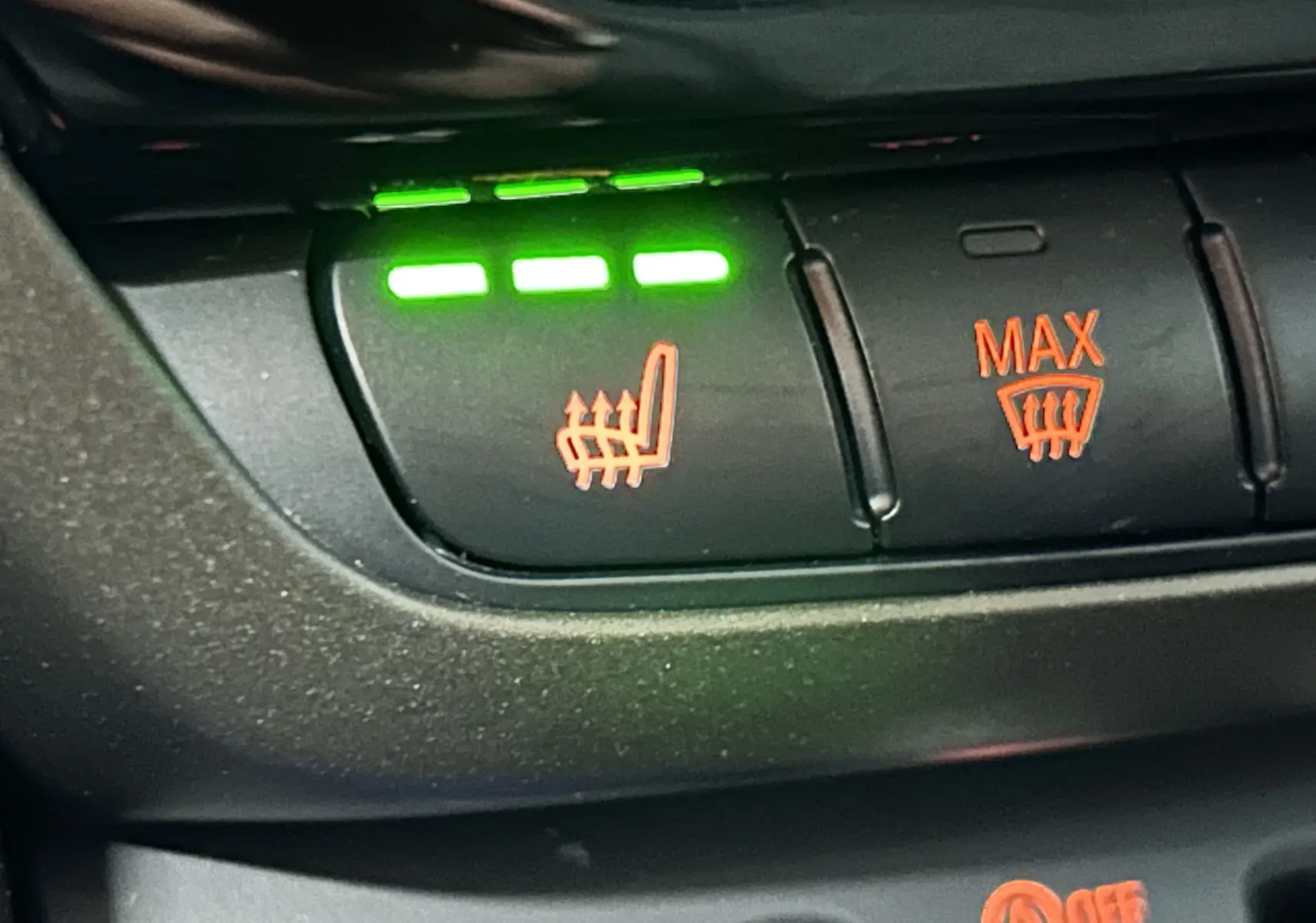 Gros plan sur les boutons de commande du siège chauffant et du dégivrage avant dans une MINI Countryman vert métallique.