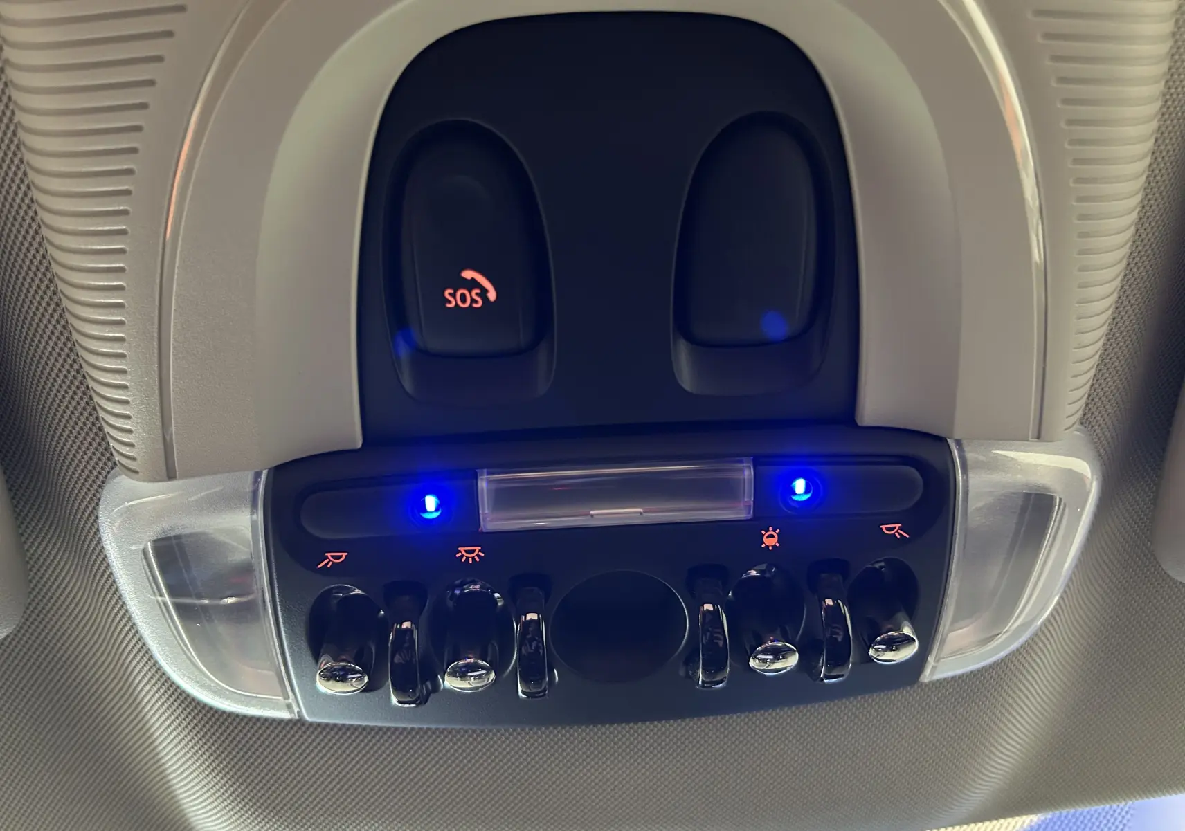 Vue en gros plan du panneau de commandes intérieures avec interrupteurs chromés et boutons SOS éclairés en bleu sur MINI Countryman 2021.