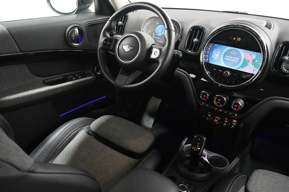 Vue intérieure côté conducteur du MINI Countryman 2021 avec tableau de bord noir, écran central rond et éclairage d'ambiance bleu.