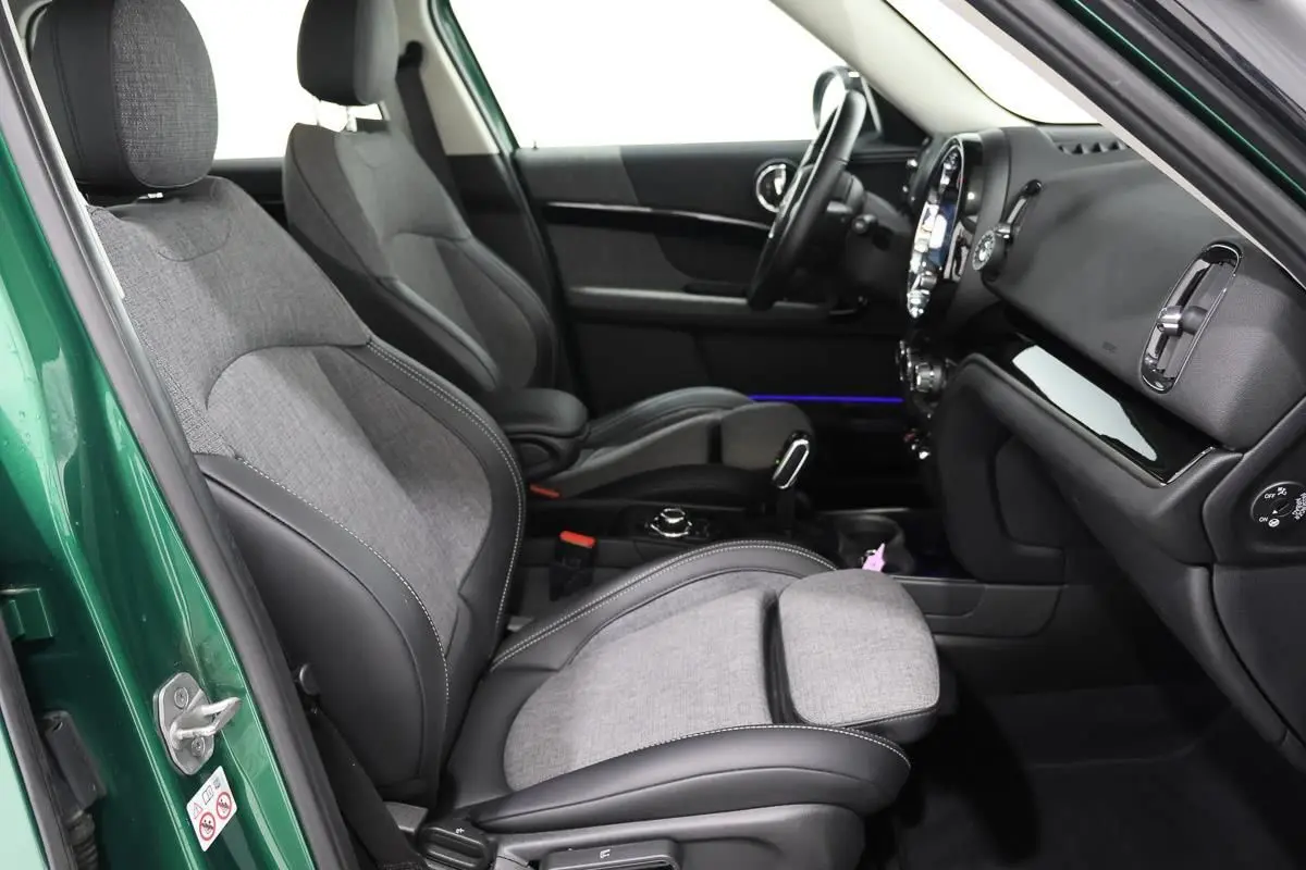 Intérieur avant droit d'une MINI Countryman vert métallisé, sièges tissu gris et cuir noir avec console centrale visible.
