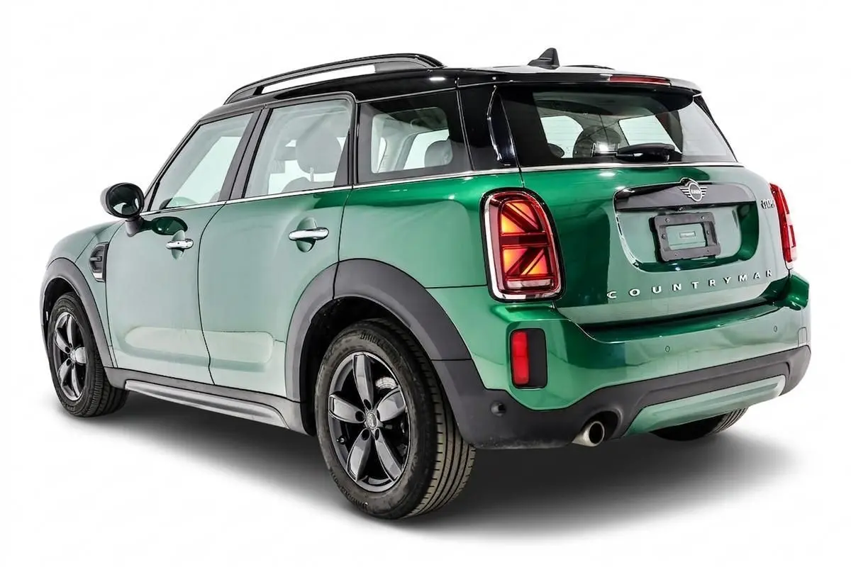 Vue 3/4 arrière droit d'une MINI Countryman vert métallisé avec toit noir et feux arrière Union Jack allumés.