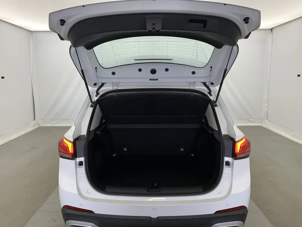Vue arrière du MG ZS blanc Dover White 2026 avec coffre ouvert et feux arrière allumés dans un espace neutre.